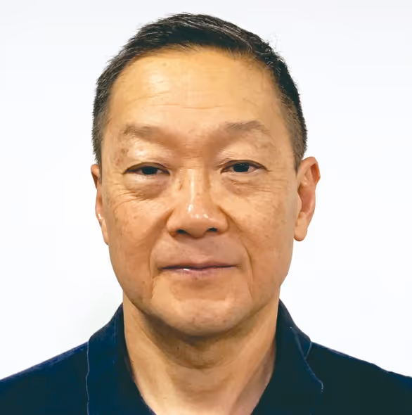 Retrato de homem asiático de meia-idade com cabelo curto e camisa escura, olhando para a câmera com expressão neutra.