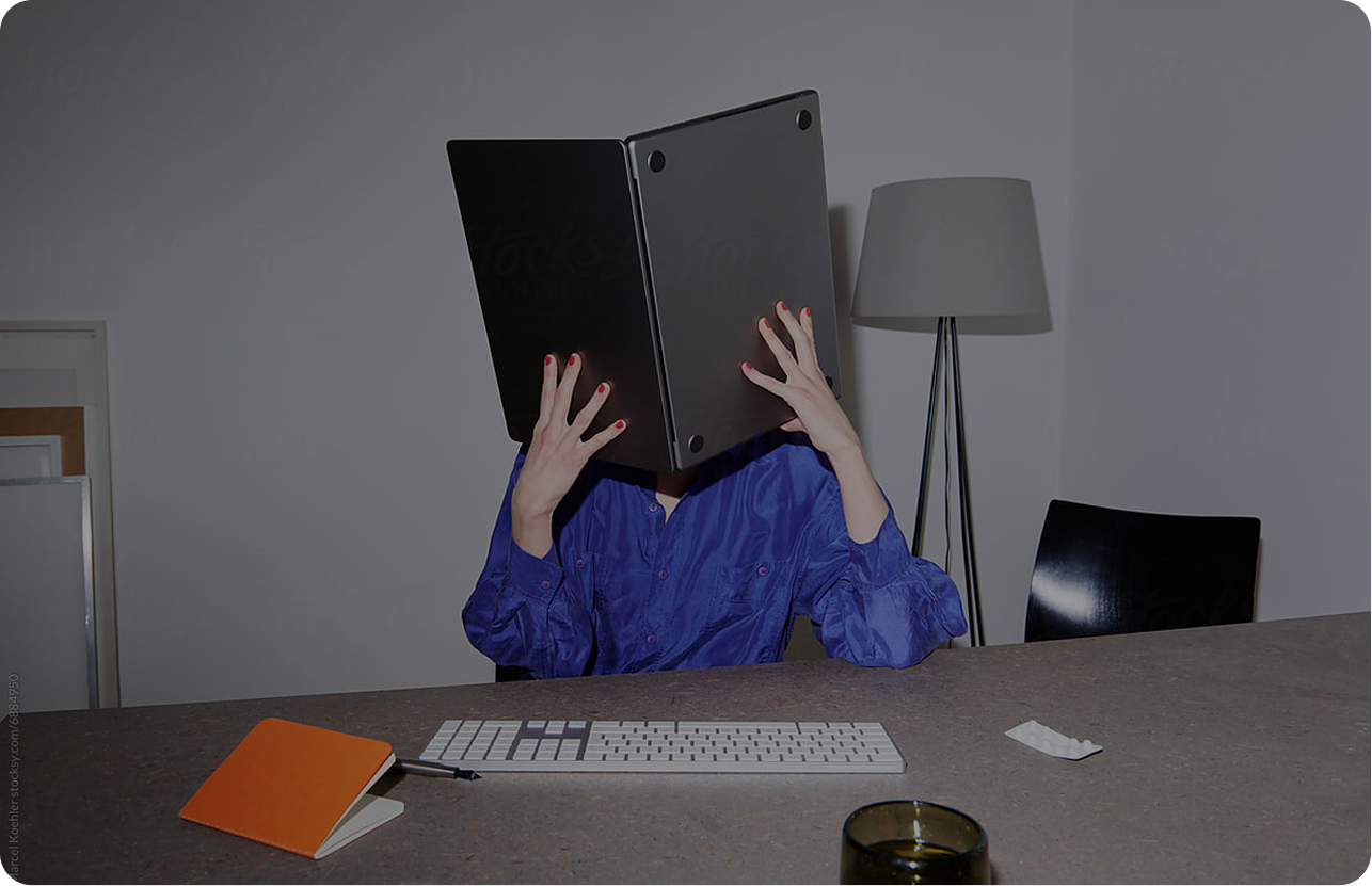 Woman at a desk holding a laptop over her head