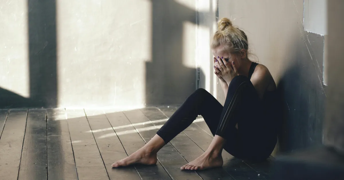Young woman sitting on the floor and crying alone, showing emotional pain from PTSD and anxiety.