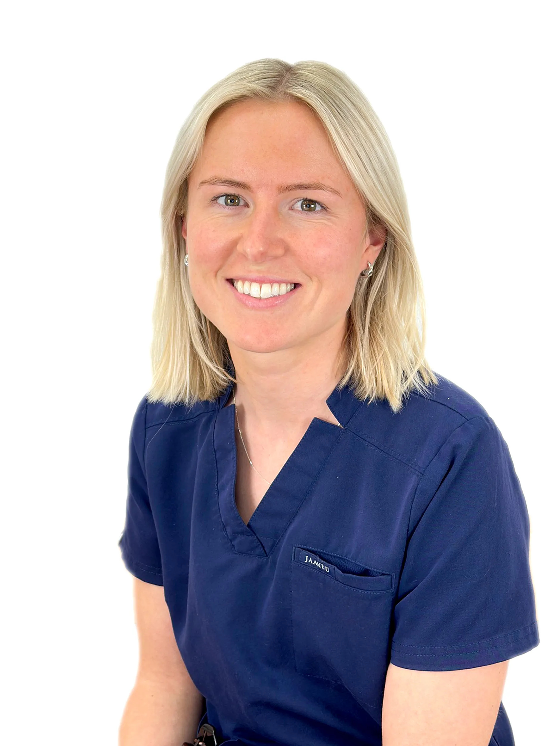 Smiling woman with blonde hair wearing navy blue medical scrubs with a pocket on the chest and small earrings.