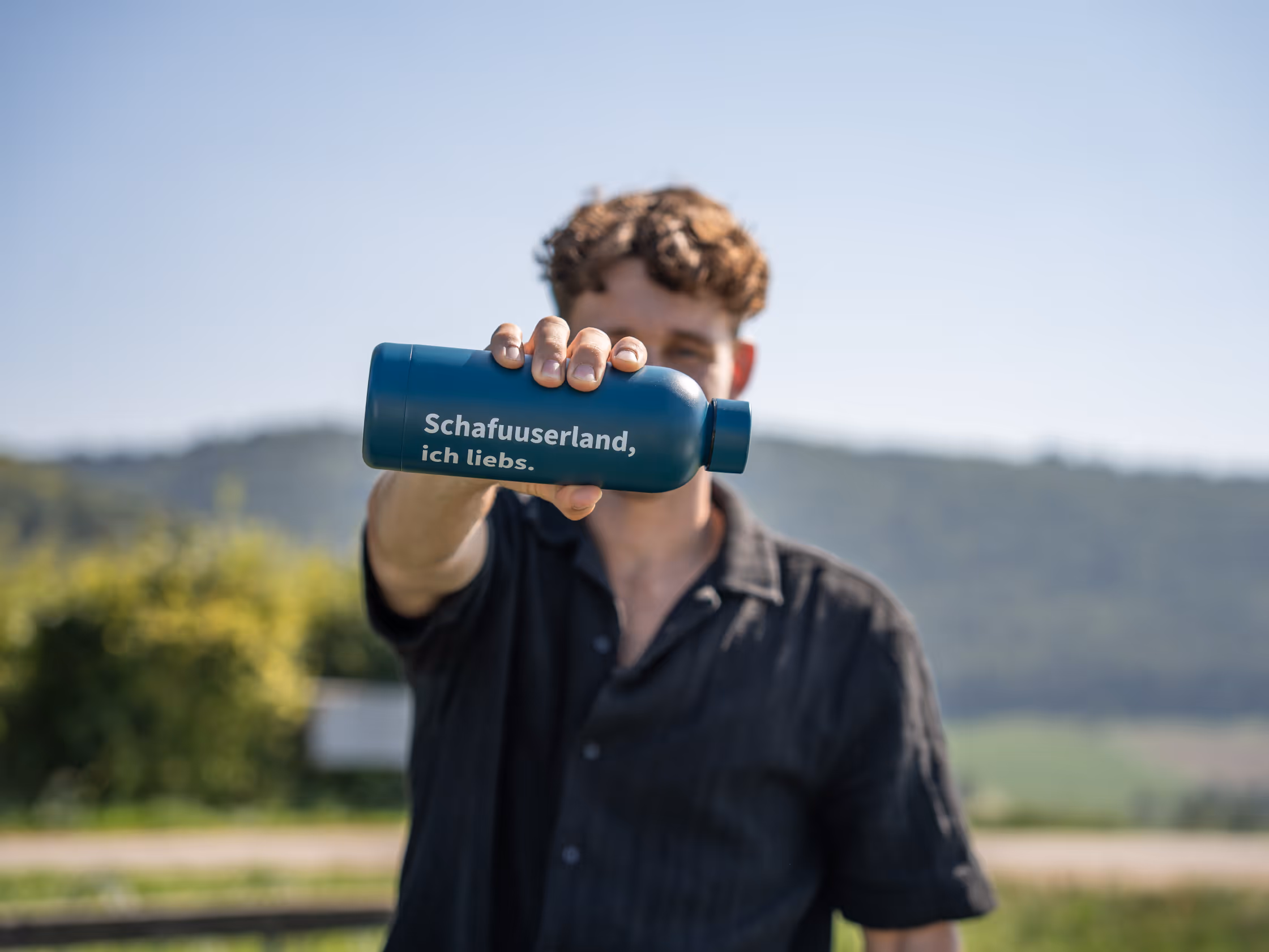 Eiskunstlauf Europameister Lukas Britschgi hält eine gebrandete Flasche von Schaffhauserland Tourismus in die Kamera