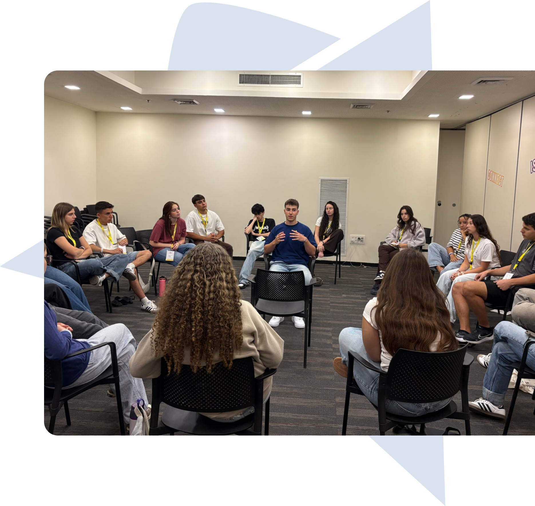 A group of young people sitting in a circle in a meeting room, engaged in a discussion with one person speaking in the center.