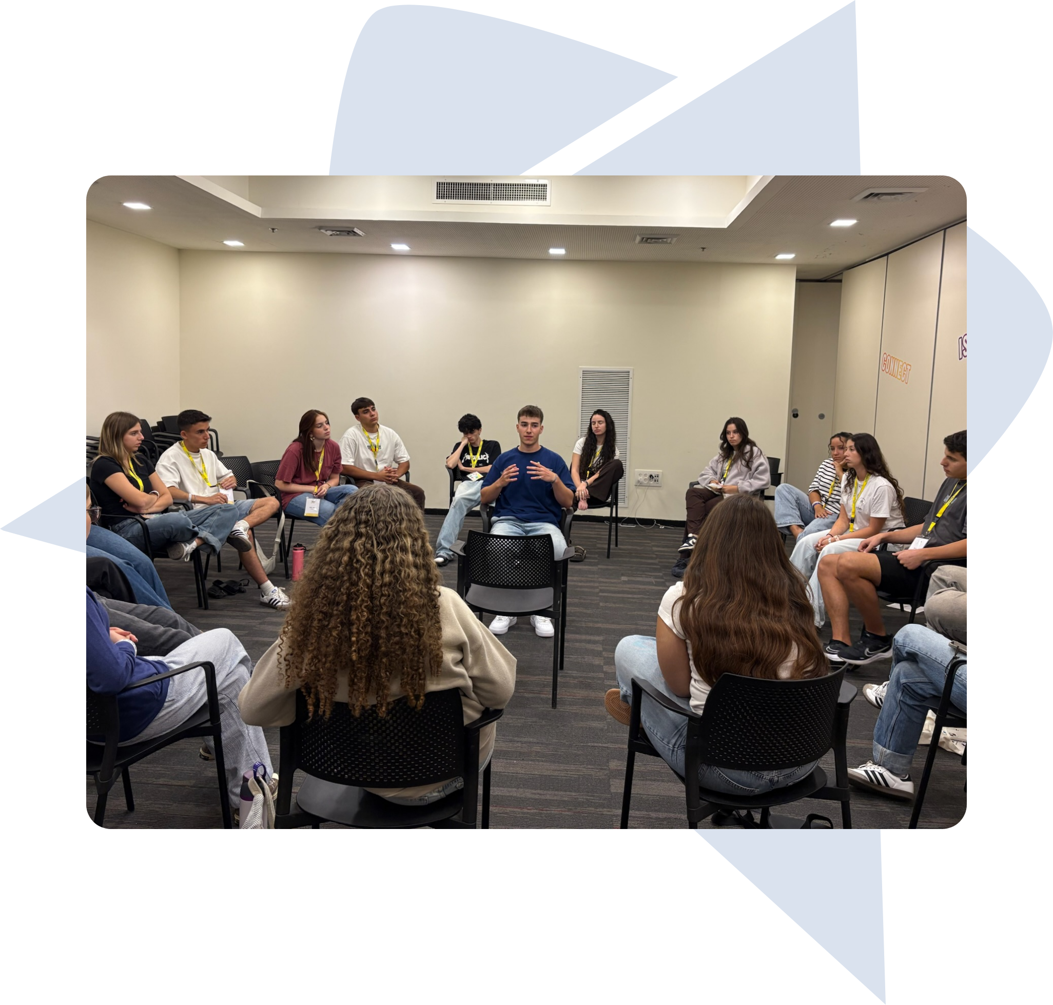 A group of young people sitting in a circle in a meeting room, engaged in a discussion with one person speaking in the center.