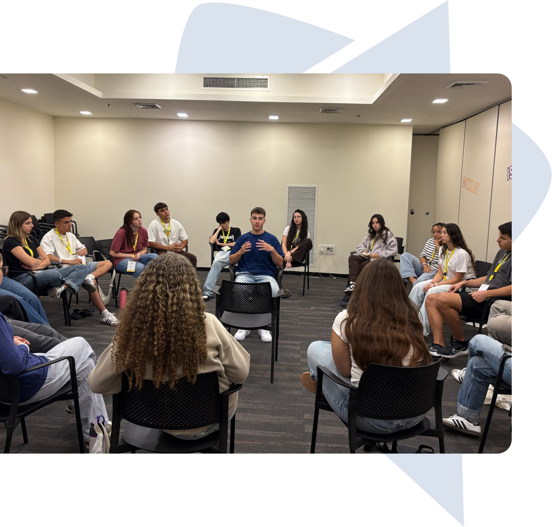 A group of young people sitting in a circle in a meeting room, engaged in a discussion with one person speaking in the center.