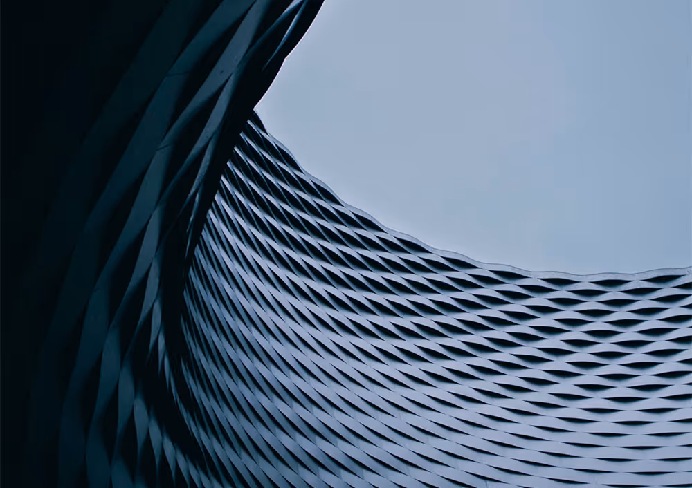 Curved architectural structure with a textured diamond pattern opening to a pale blue sky.