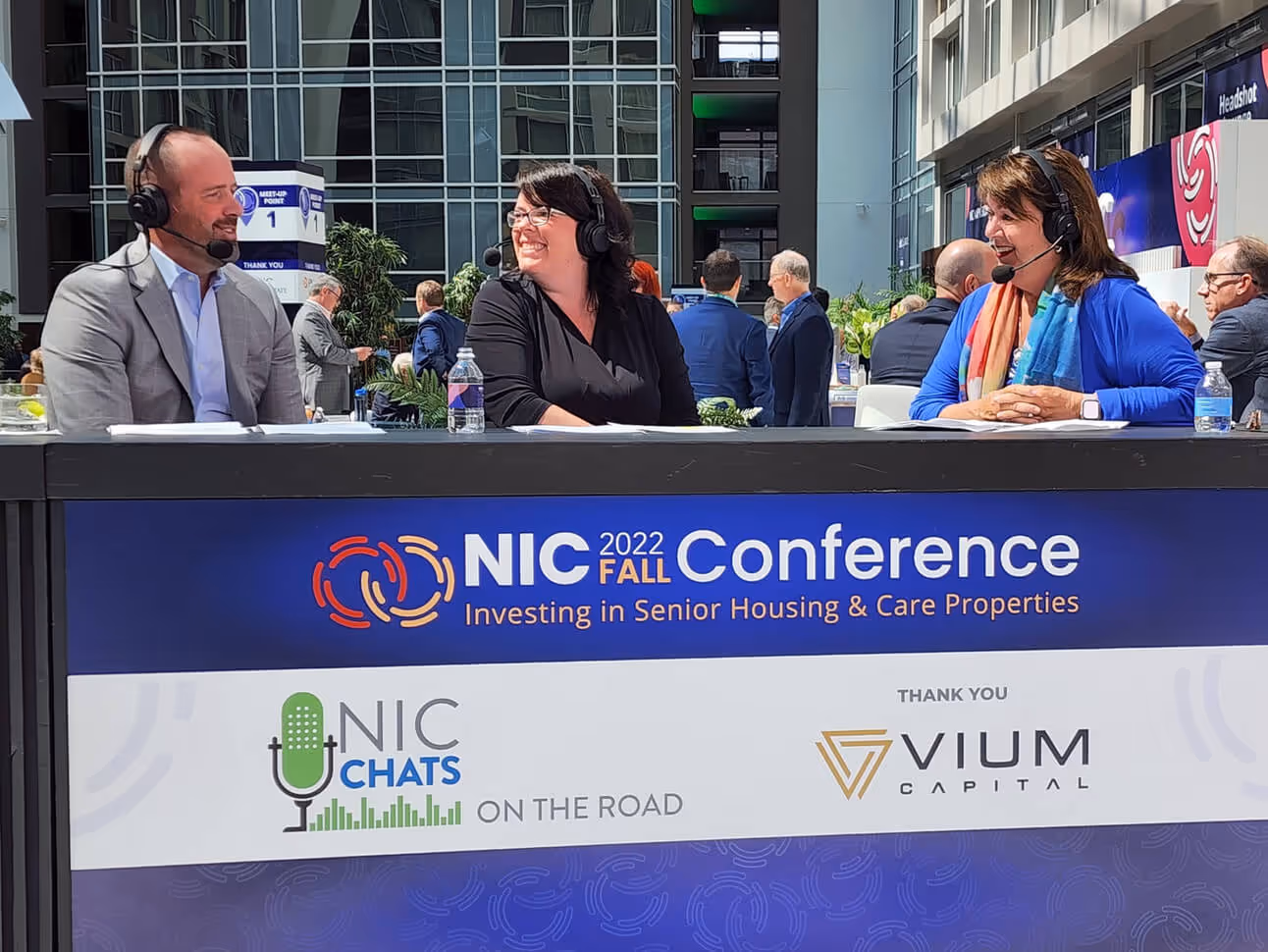 Three people wearing headsets talk behind a desk at the NIC 2022 Fall Conference on senior housing and care properties.