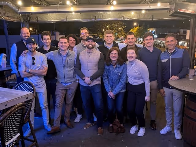 Group of twelve people posing and smiling together outdoors at night under a covered patio with string lights.