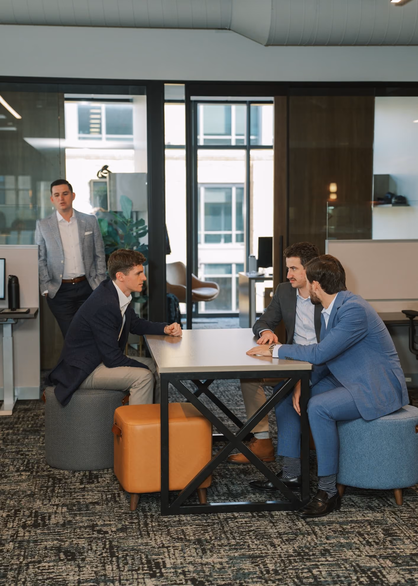 Four men in business attire having a discussion around a table in a modern office space with glass partitions.