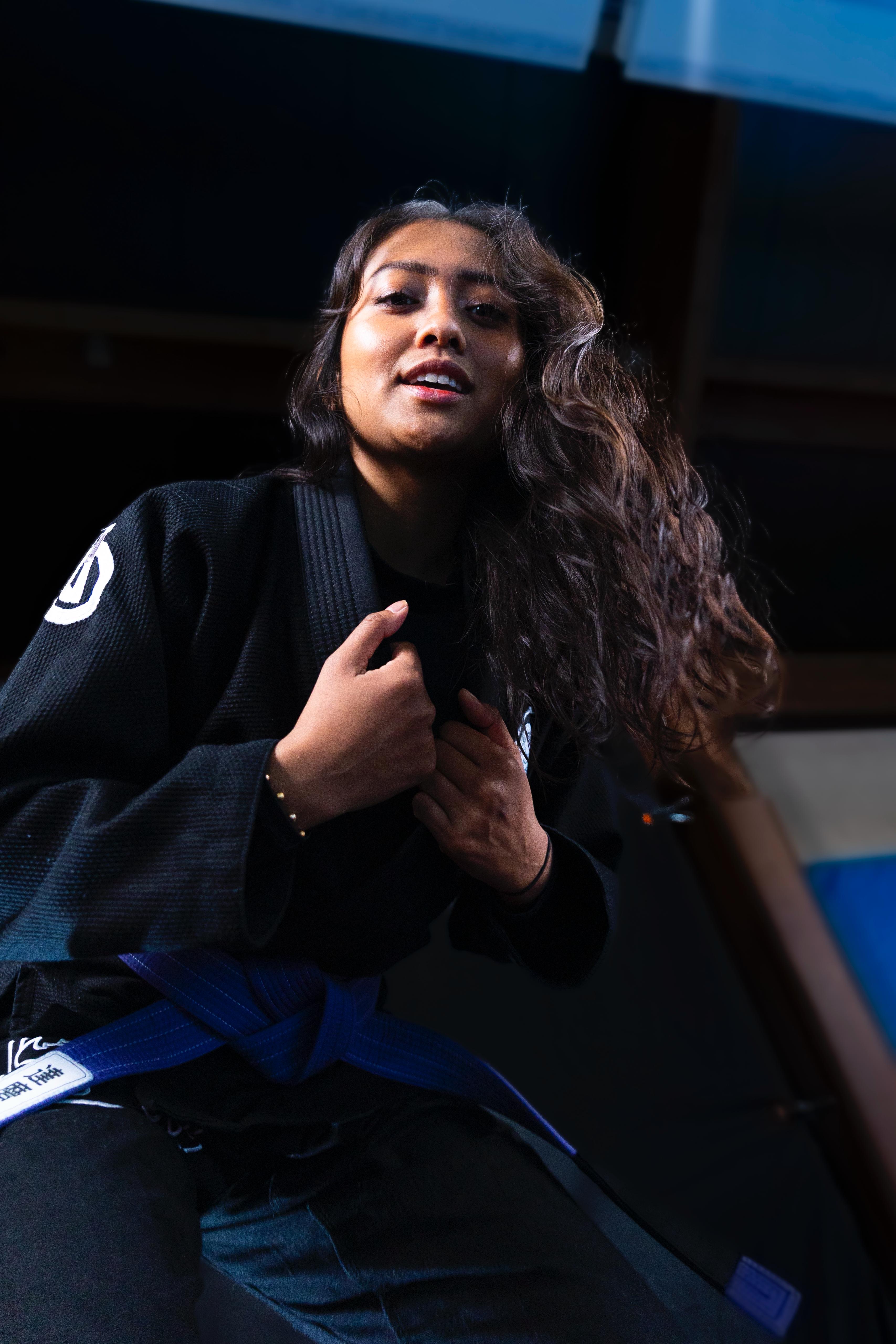 Woman in a black martial arts gi with a blue belt smiling and adjusting her collar.