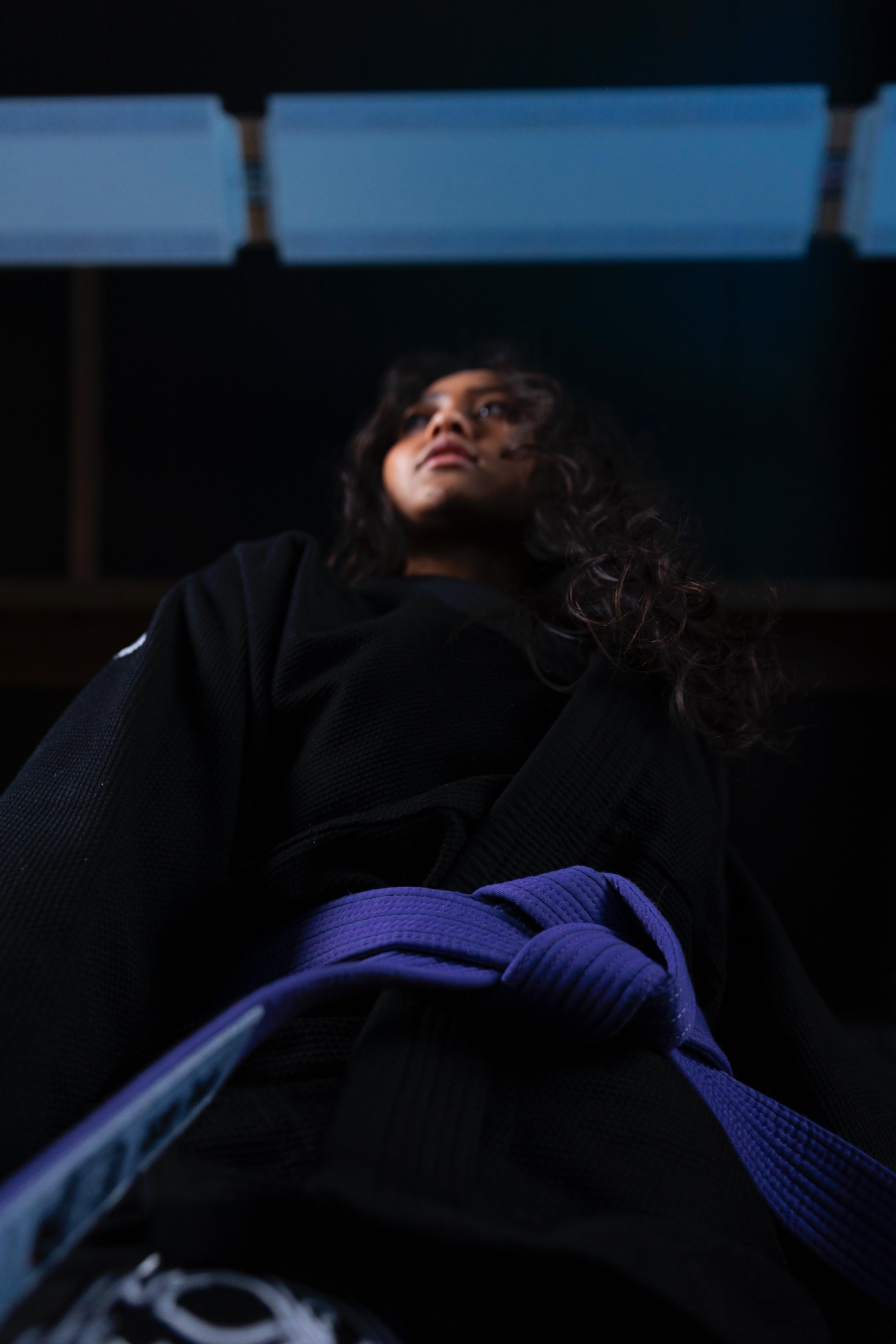 Low-angle view of a woman in a black martial arts gi with a blue belt looking forward.