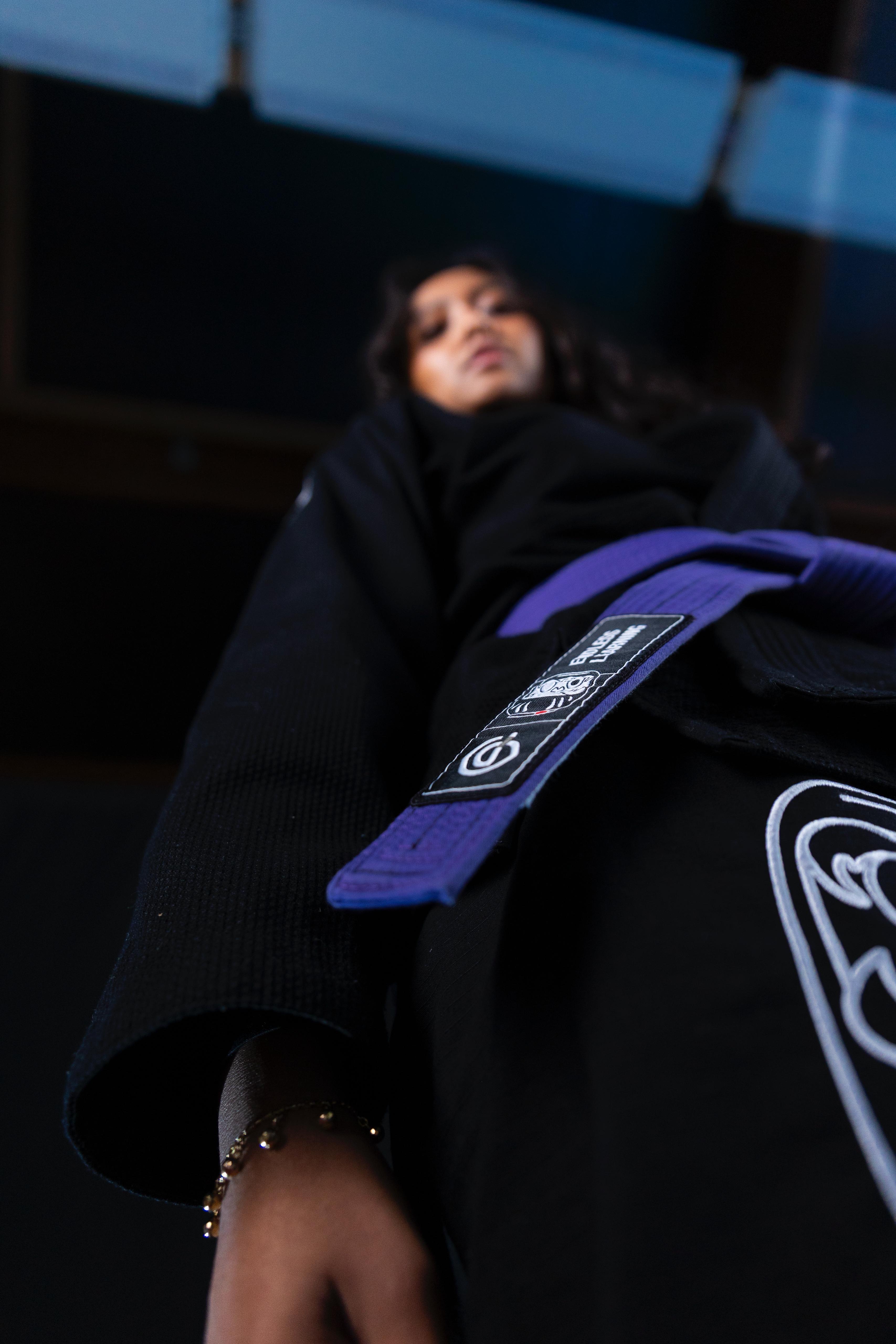 Low-angle view of a person wearing a black martial arts gi with a purple belt tied around their waist.