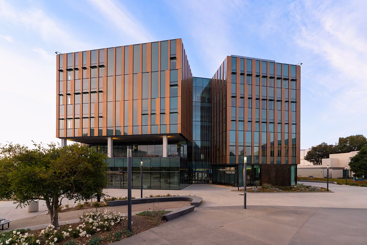 Viterbi Family Vision Research Center at Shiley Eye Institute. Modern multi-story building with vertical orange and glass panels under a partly cloudy sky.