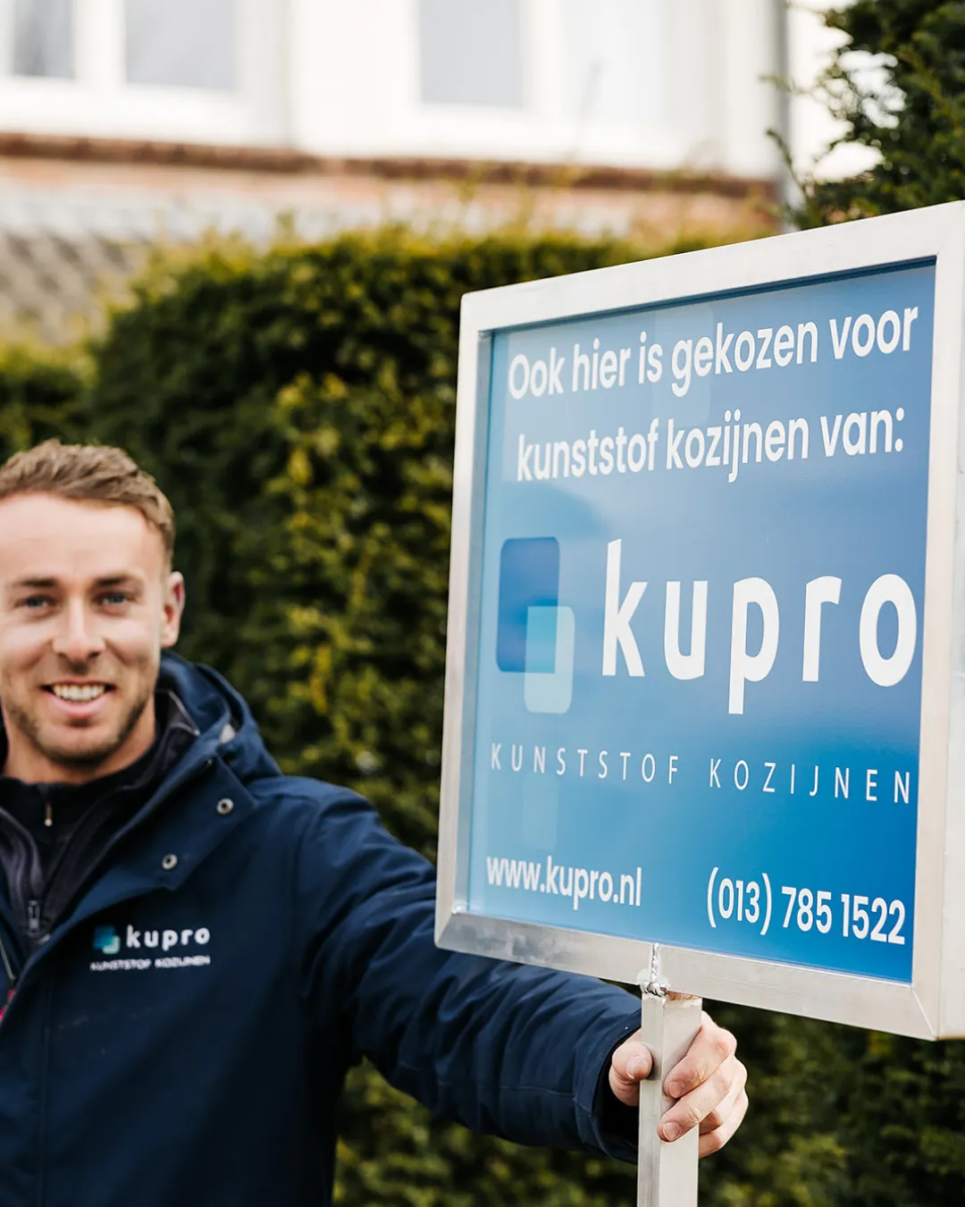 Kupro-medewerker naast een tuinbord met de tekst: ook hier is gekozen voor kunststof kozijnen van Kupro