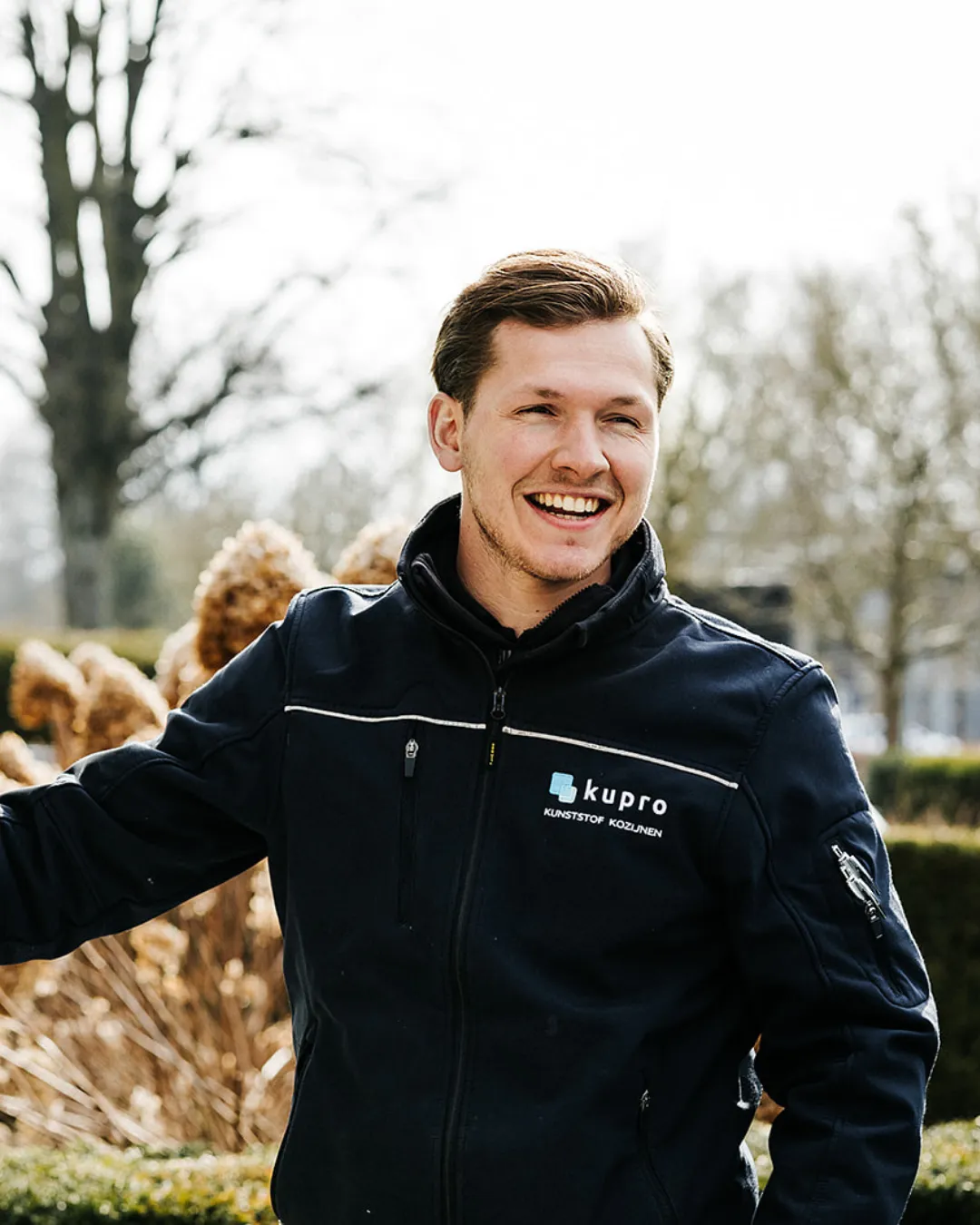 Lachende Kupro-medewerker in bedrijfsjas buiten in een tuin