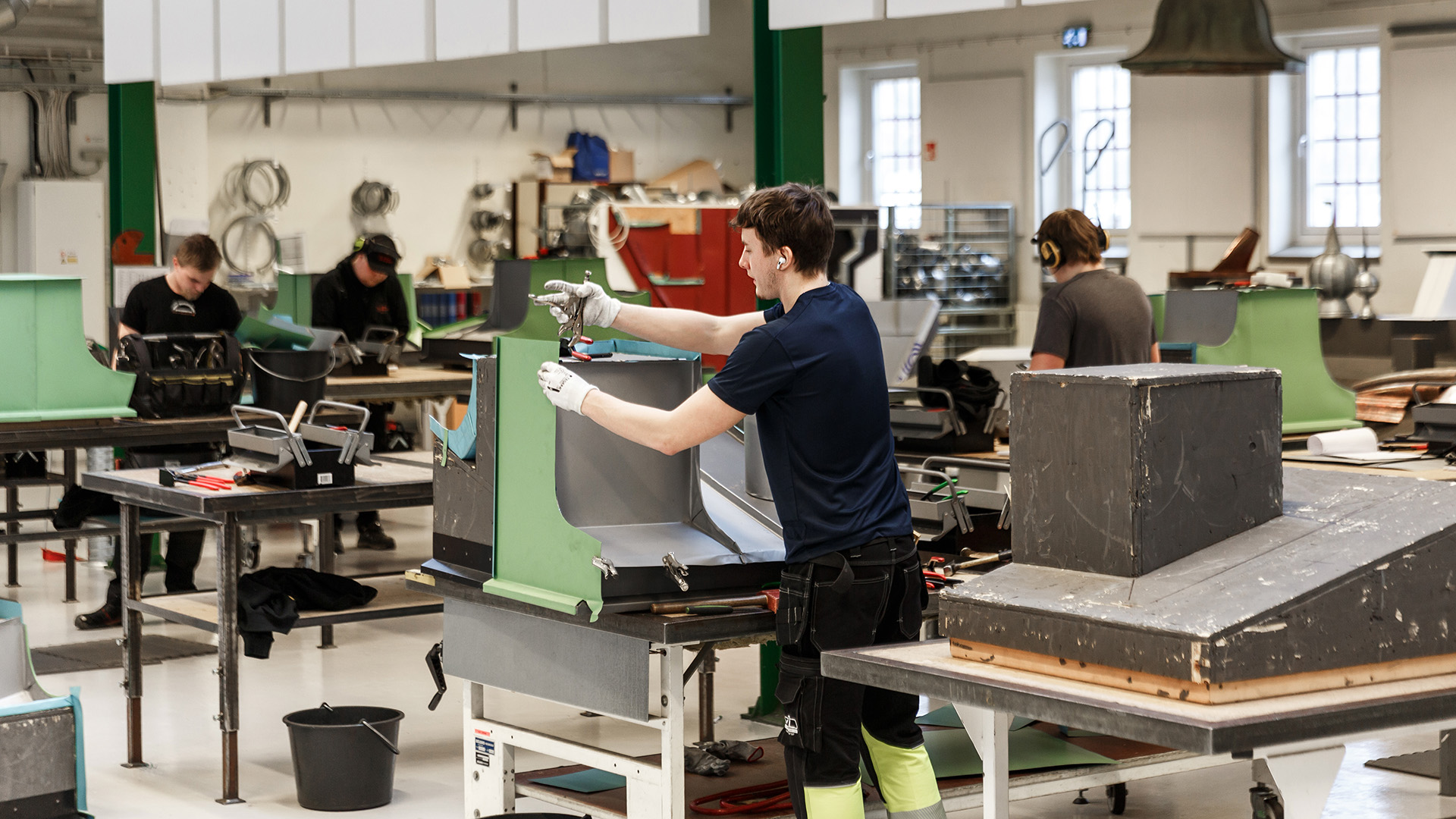 Lärling och handledare står vid ett bord i en verkstad och grejar med ett rör