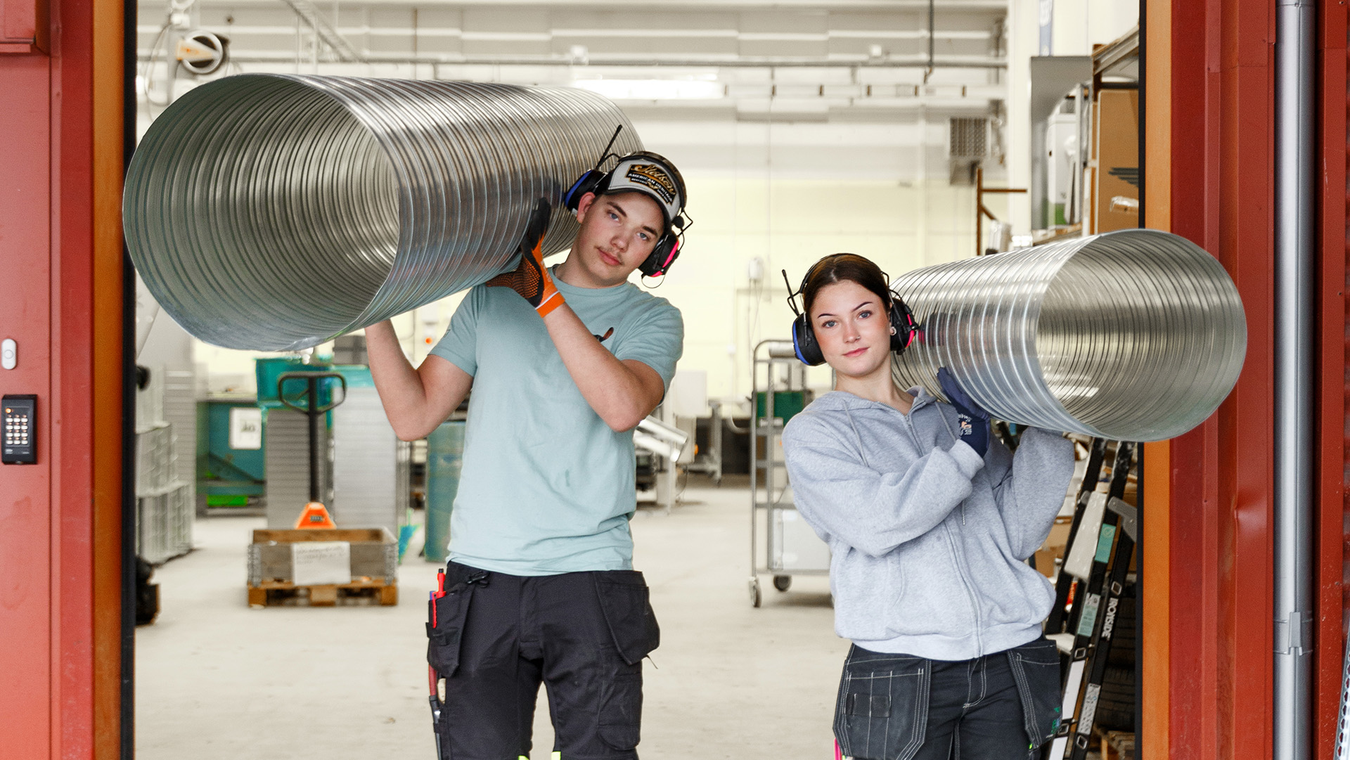 Två personer går upp för en trappa med ett rör bärandes var