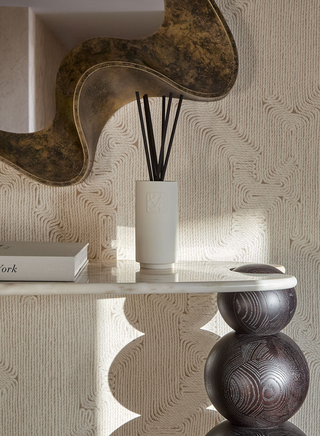 Textured wallcovering with brass abstract shape mirror. On the console sits August&Piers diffuser.