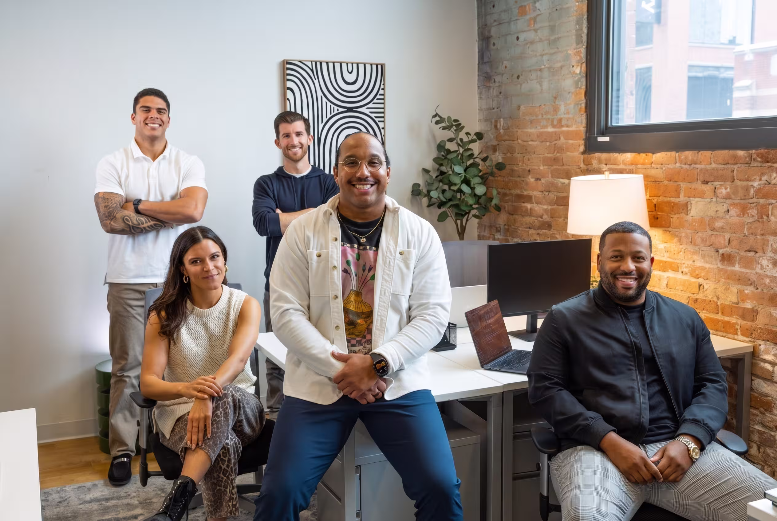 Journey Delivers team smiling in a modern office with exposed brick and computer desks.