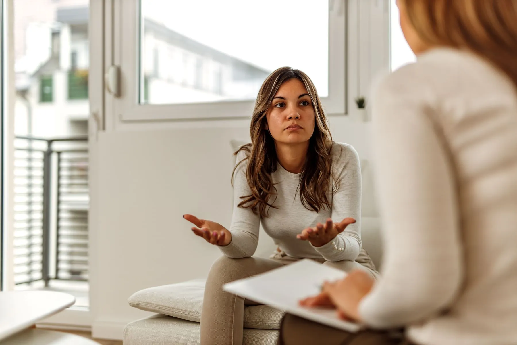 Young woman sitting on couch discussing holistic integral therapy with therapist.