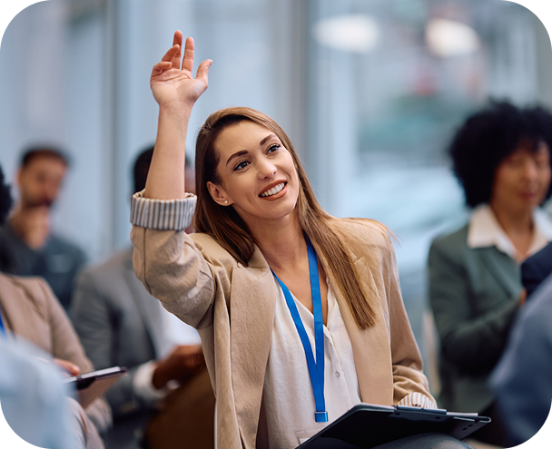 Smiling woman in business attire raising her hand during a meeting or conference.