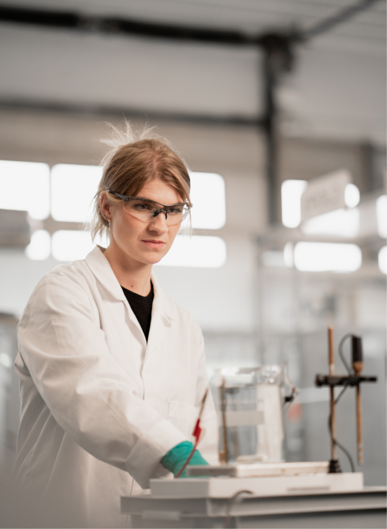 Scientist wearing safety glasses and a white lab coat conducting an experiment with lab equipment in a research laboratory.