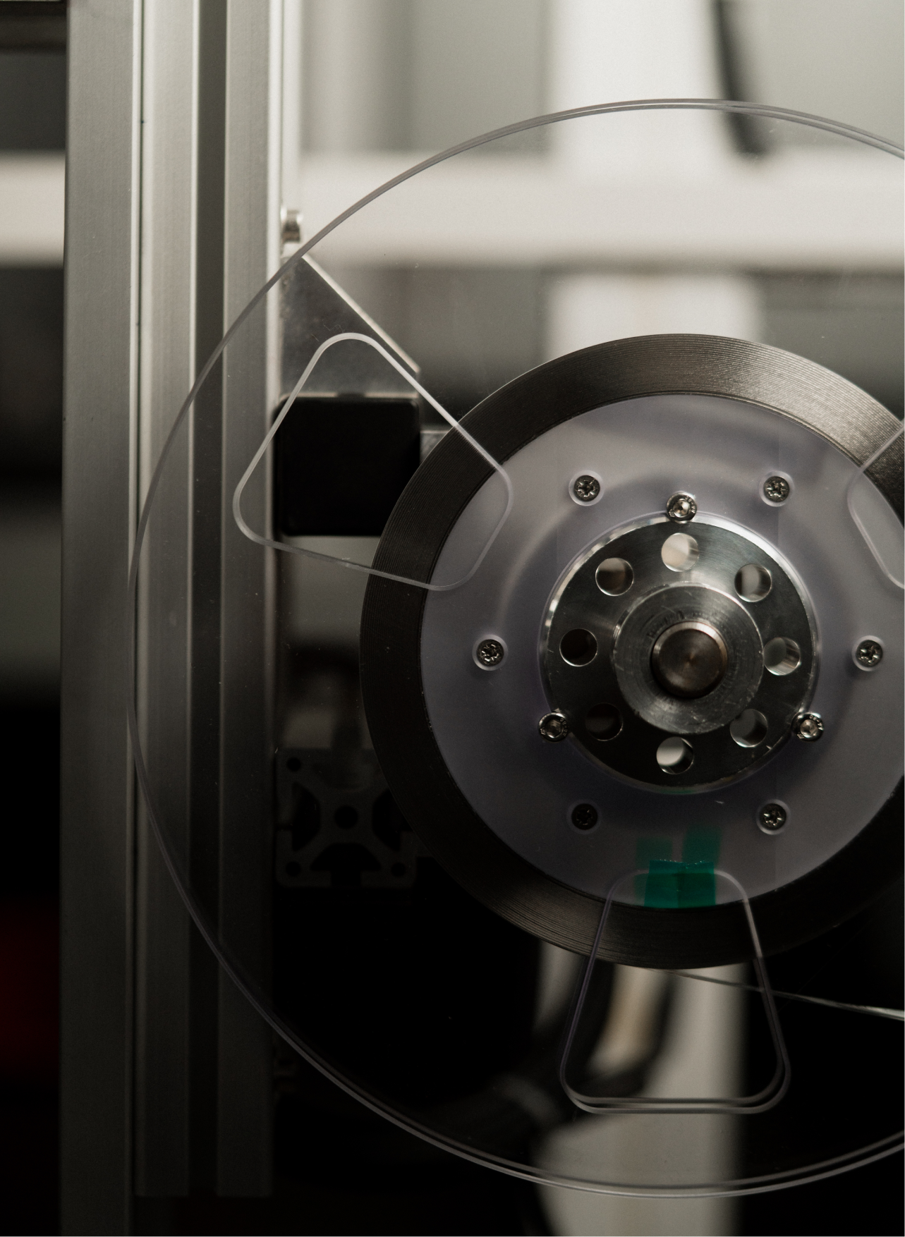 Close-up of a transparent round wheel with metal center and screws mounted on a metal frame in a lab setting.