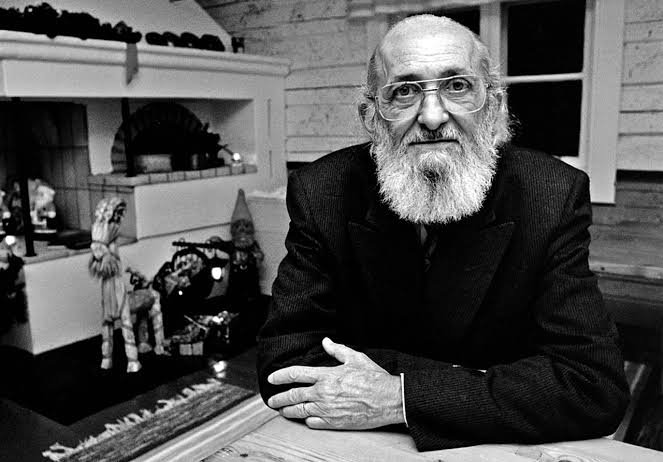 Paulo Freire in a cozy room with a neutral expression and arms crossed