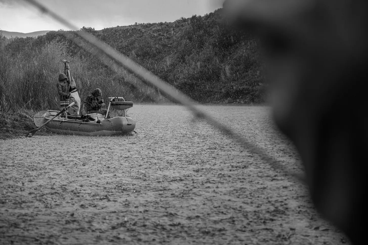 Two fly anglers on a western river caught in a giant rainstorm. They are putting on rain jackets.