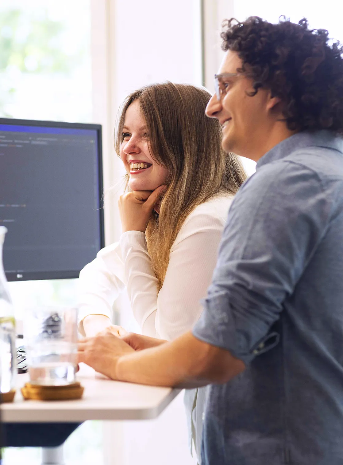 Teamwork bei CROWDCODE: zwei Mitarbeiter:innen stehen gemeinsam an einem Arbeitsplatz