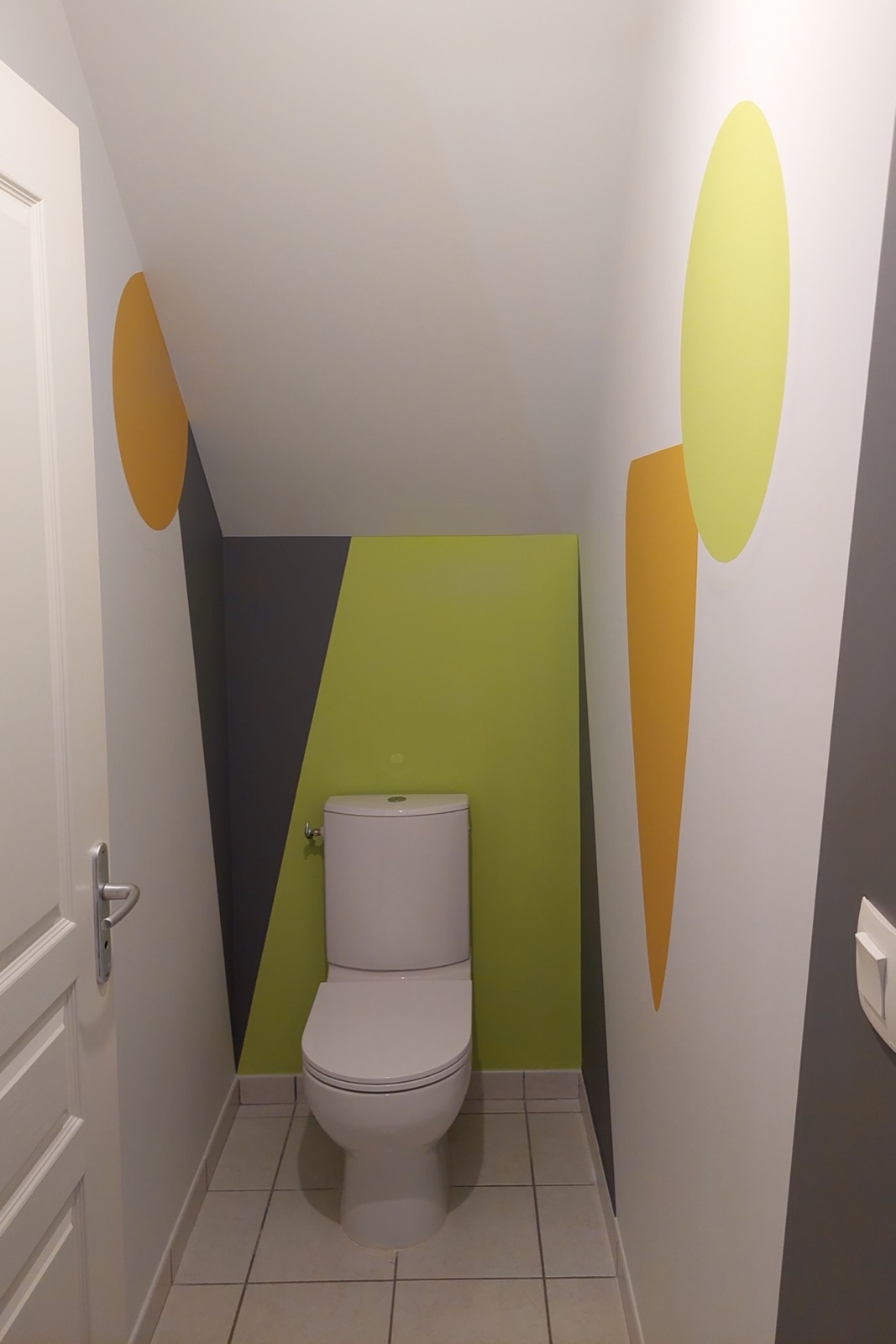 WC sous escalier décoré d'une peinture graphique aux formes jaune orangé, vert anis et gris