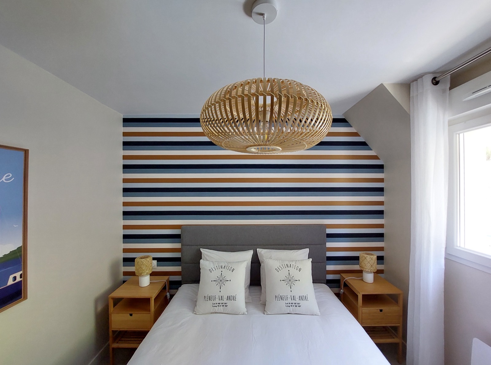Chambre sous combles avec un mur à rayures horizontales bleues, blanches et ocre derrière le lit