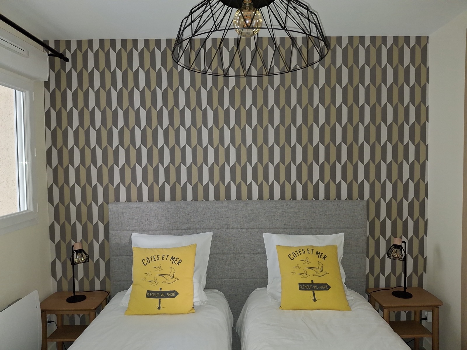 Chambre avec papier peint géométrique beige et gris derrière une tête de lit grise