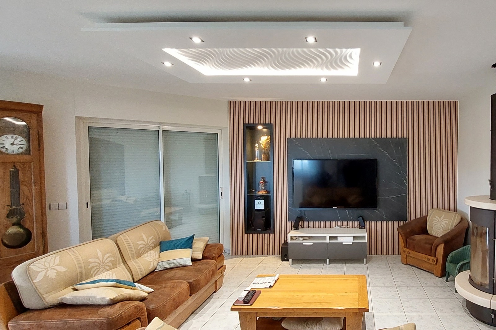 Faux plafond lumineux en staff au-dessus d'un salon, mur TV habillé de tasseaux de bois