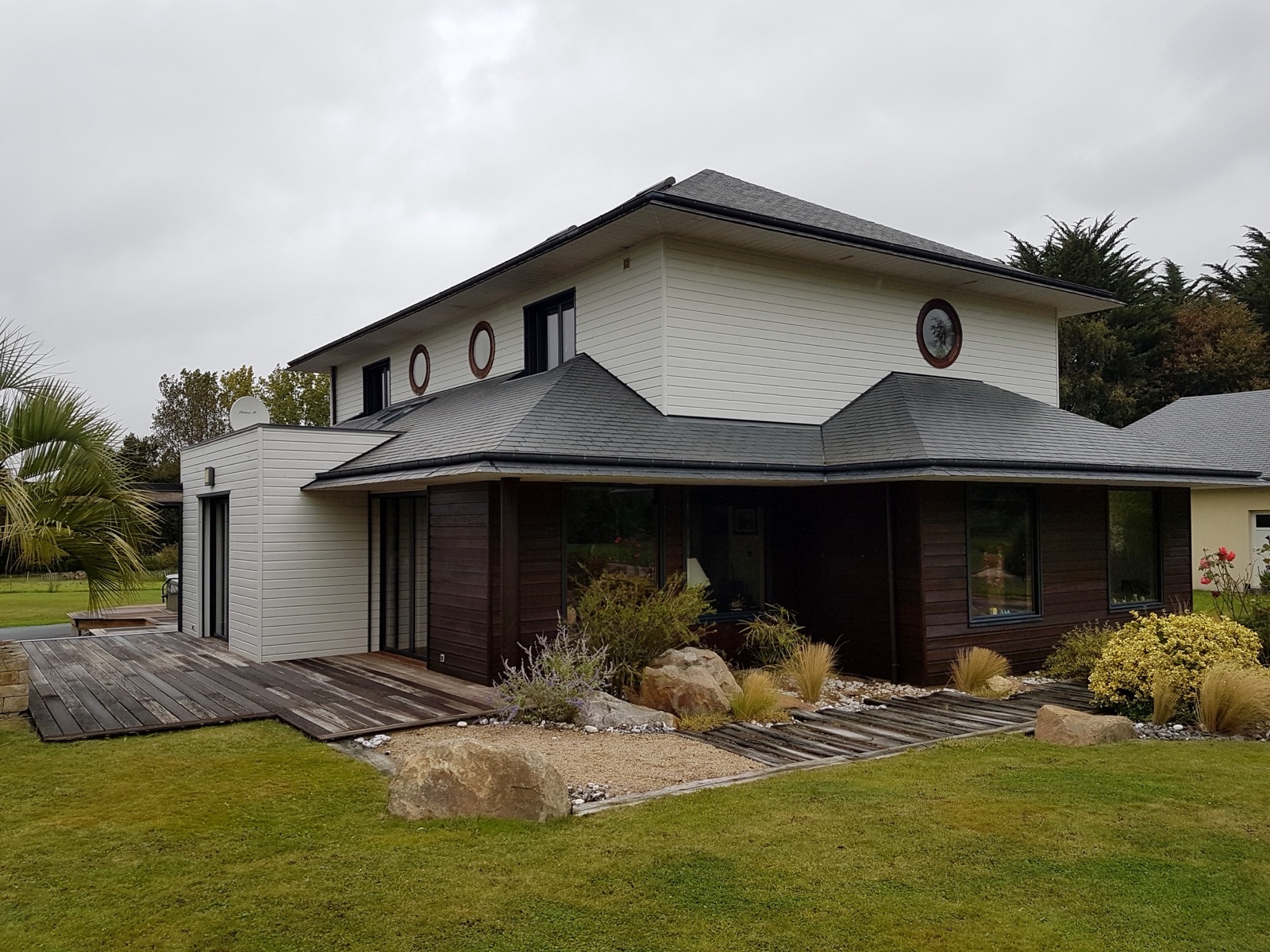 Maison contemporaine avec bardage blanc à l'étage, bardage bois sombre au rez-de-chaussée et toiture ardoise