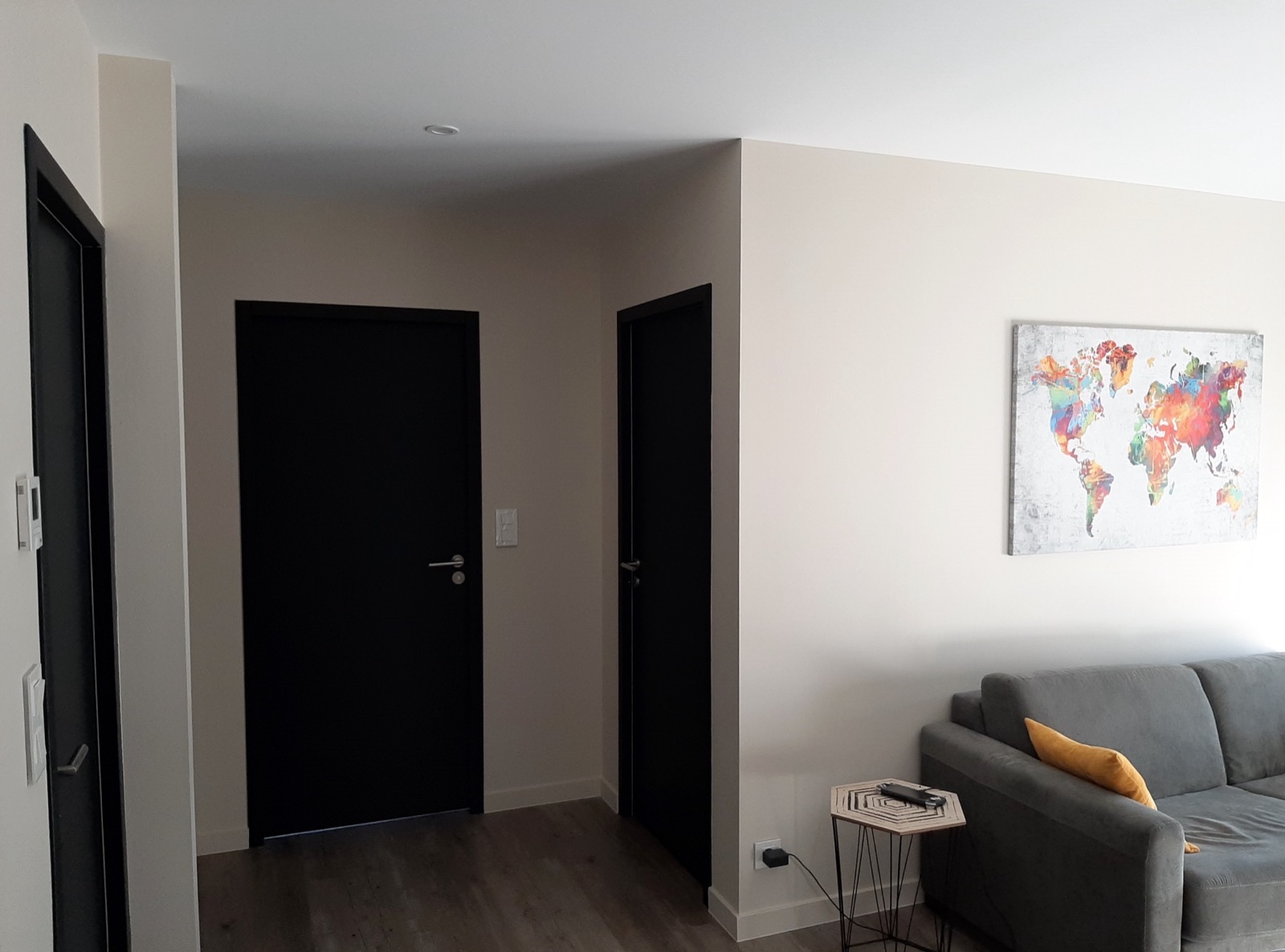 Entrée aux murs blancs avec portes intérieures peintes en noir et sol effet bois gris
