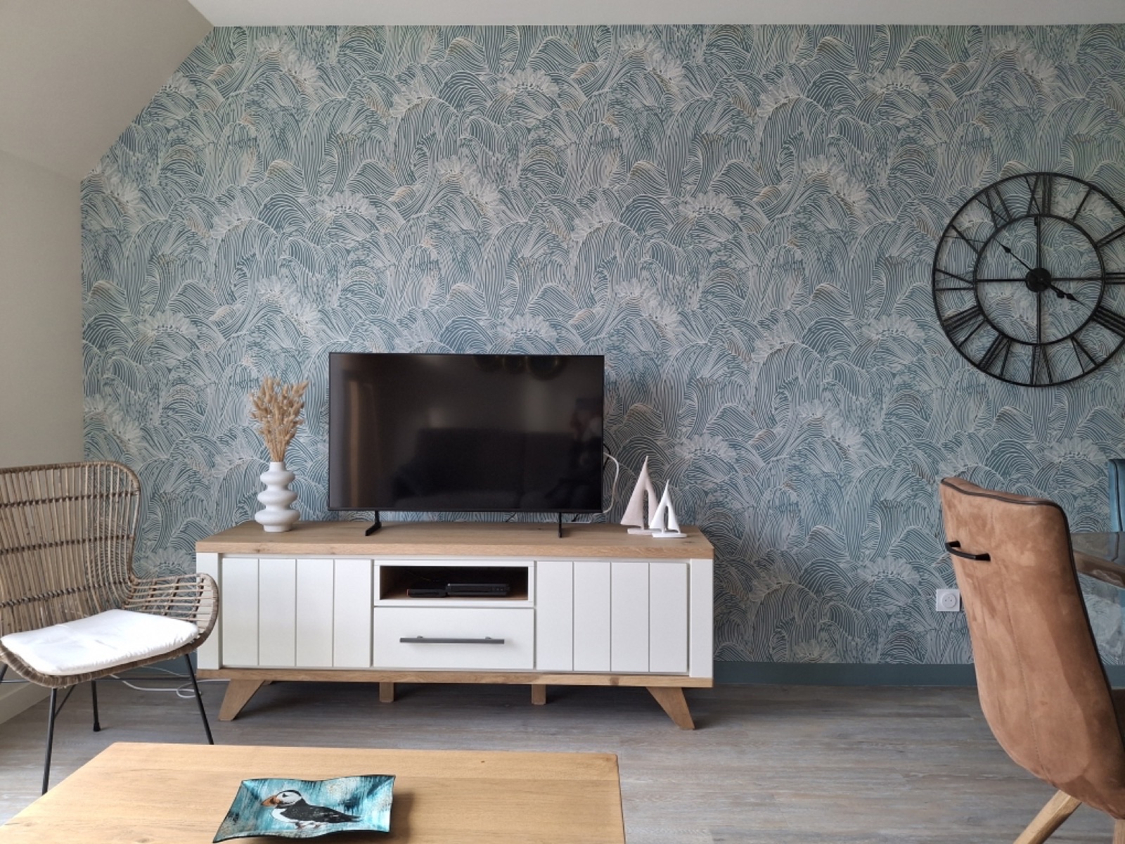 Salon avec papier peint à motif de feuilles bleu clair derrière un meuble TV blanc