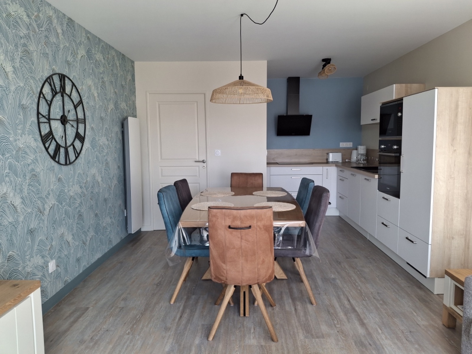 Cuisine ouverte avec papier peint à feuillage bleu, mur bleu uni et grande table