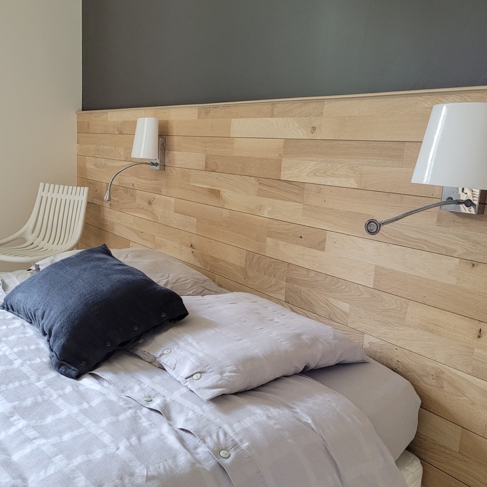 Tête de lit en lambris de bois clair à mi-hauteur, appliques murales et mur gris foncé
