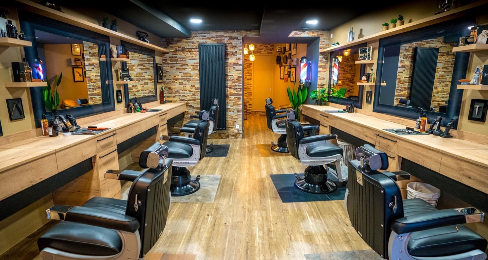Salon de coiffure-barbier avec sol en bois, murs en parement brique et fauteuils noirs