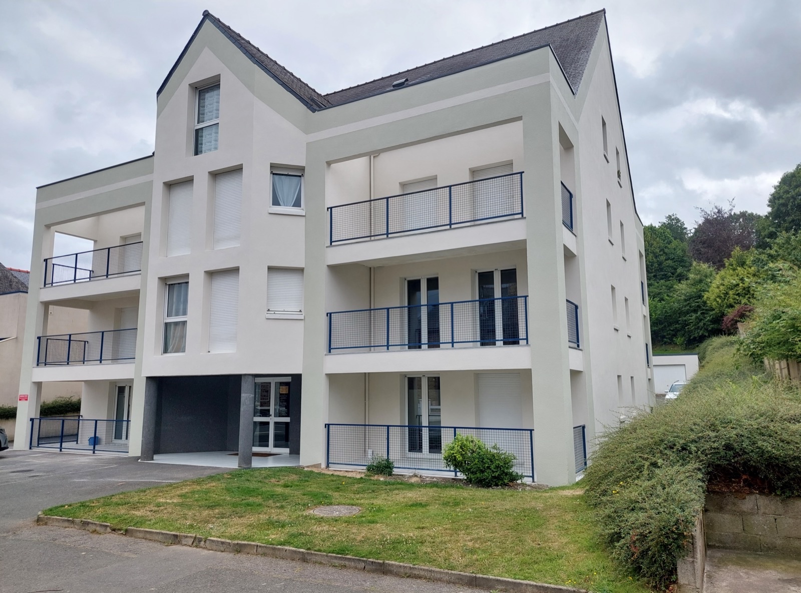 Immeuble résidentiel à façade blanche avec balcons et garde-corps noirs, pelouse au premier plan