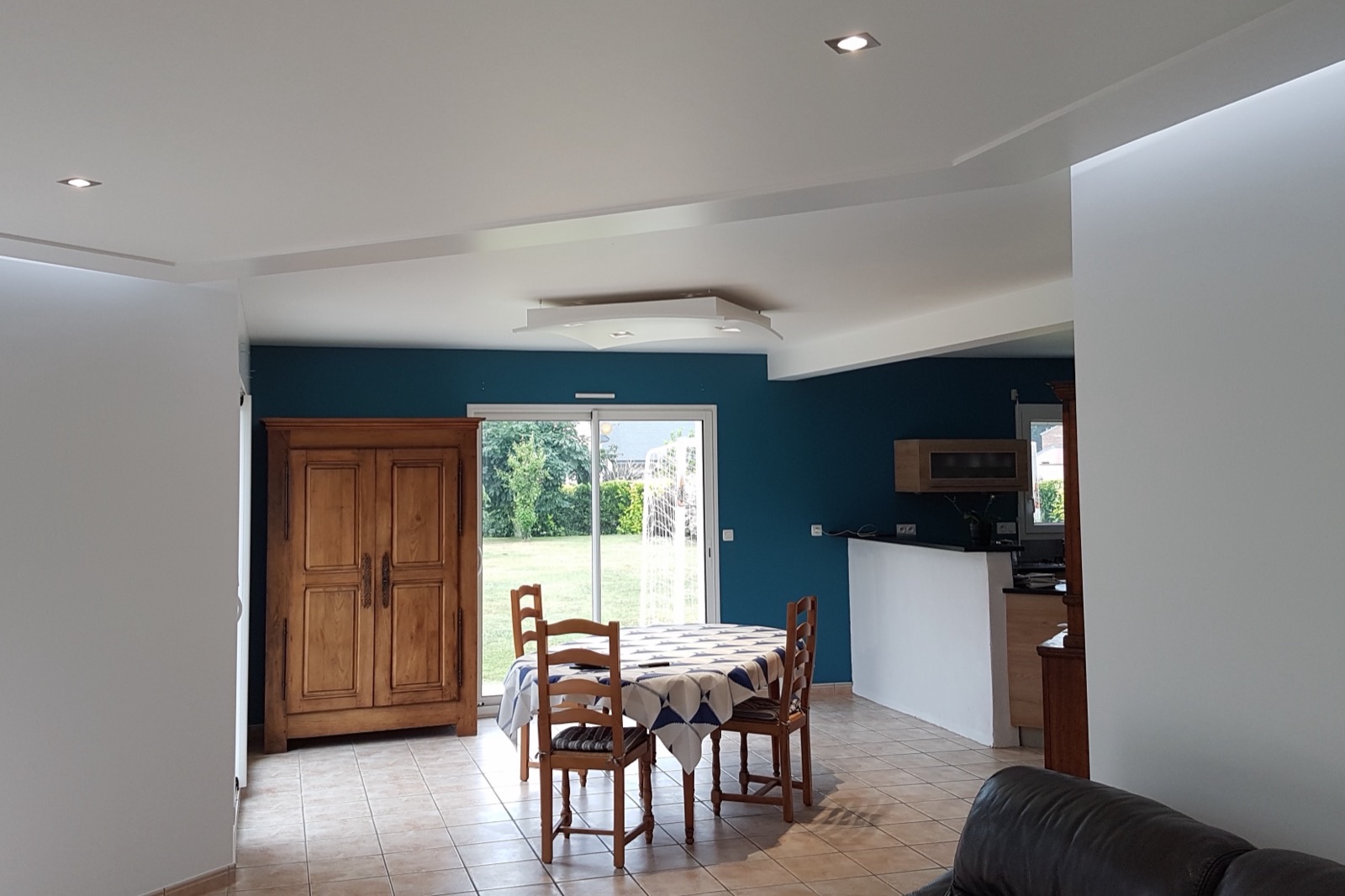 Séjour ouvert avec mur bleu canard derrière la table et caisson de plafond