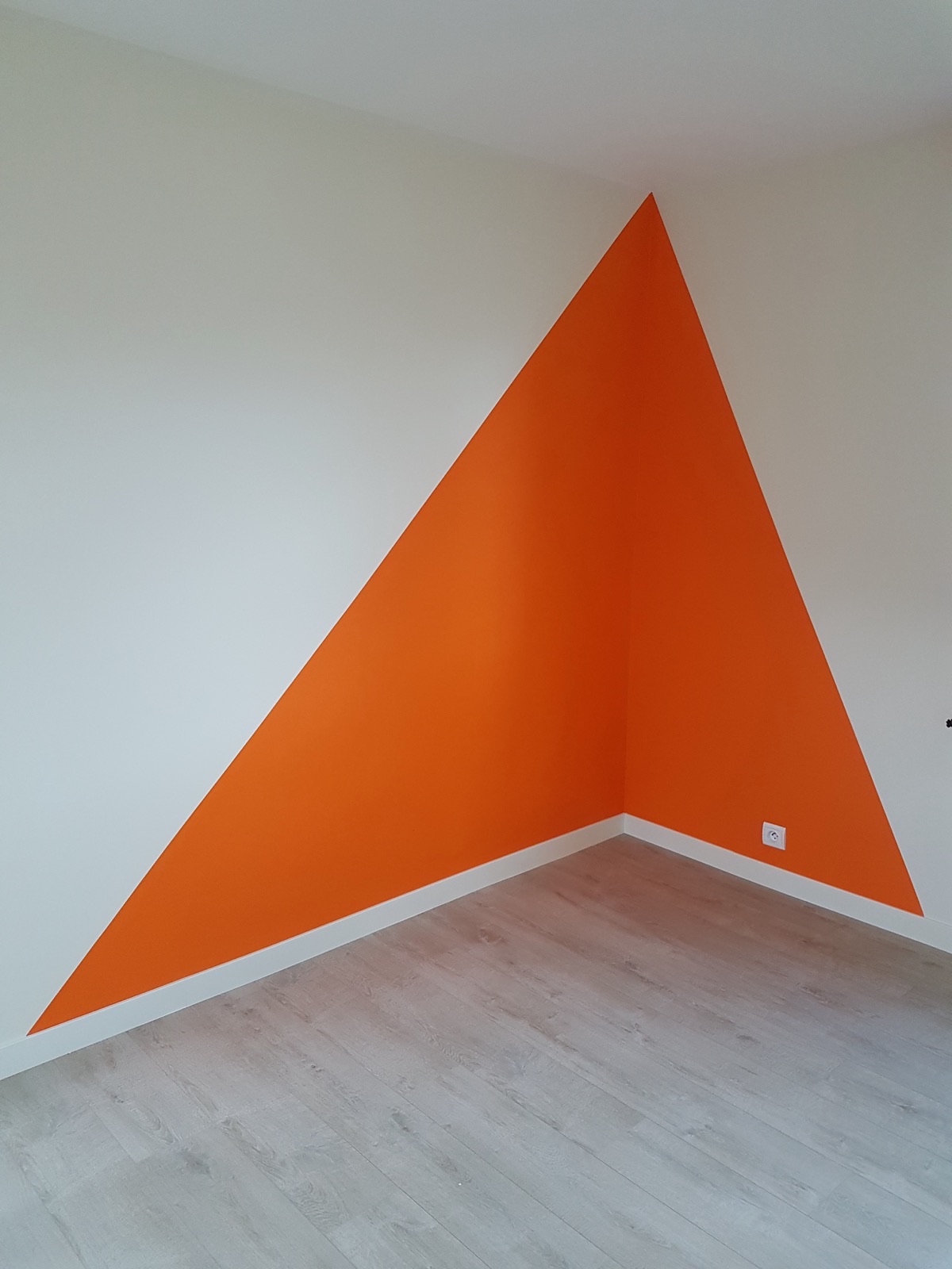 Grand triangle orange peint à cheval sur deux murs blancs dans un angle de pièce