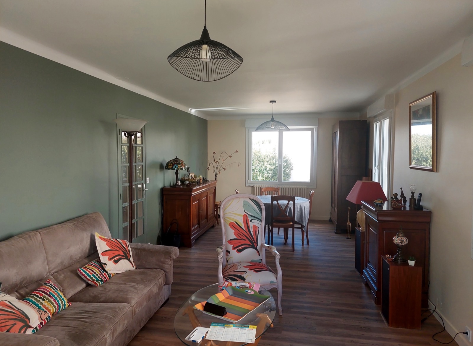 Salon avec un long mur peint en vert sauge et meubles en bois foncé