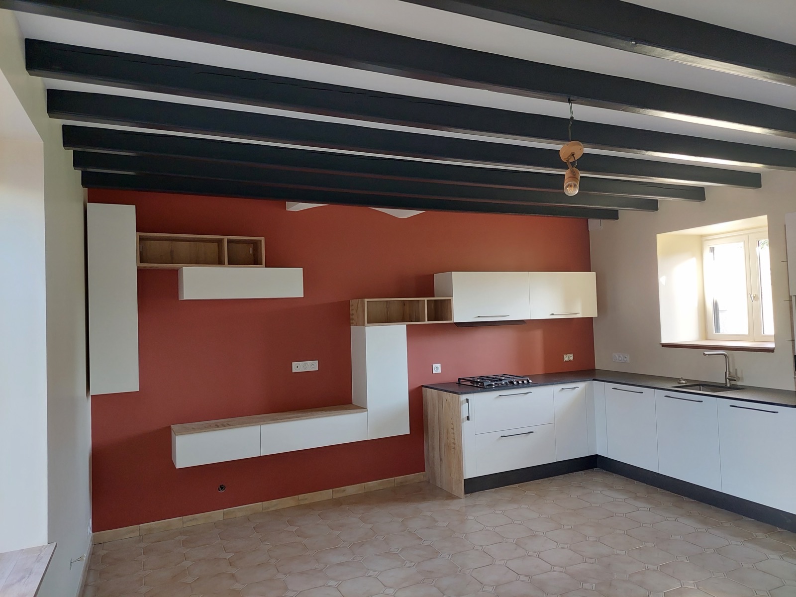 Cuisine aux poutres apparentes peintes en noir, mur terracotta et meubles blancs