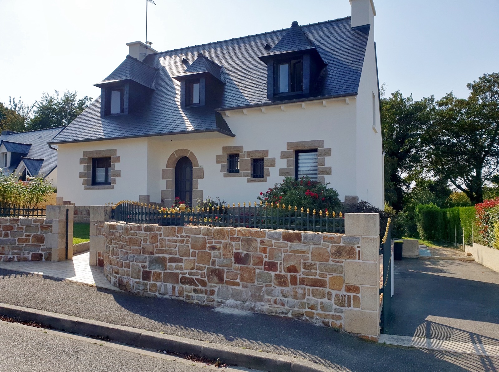 Maison à façade blanche avec encadrements en pierre, lucarnes et muret de clôture en pierre
