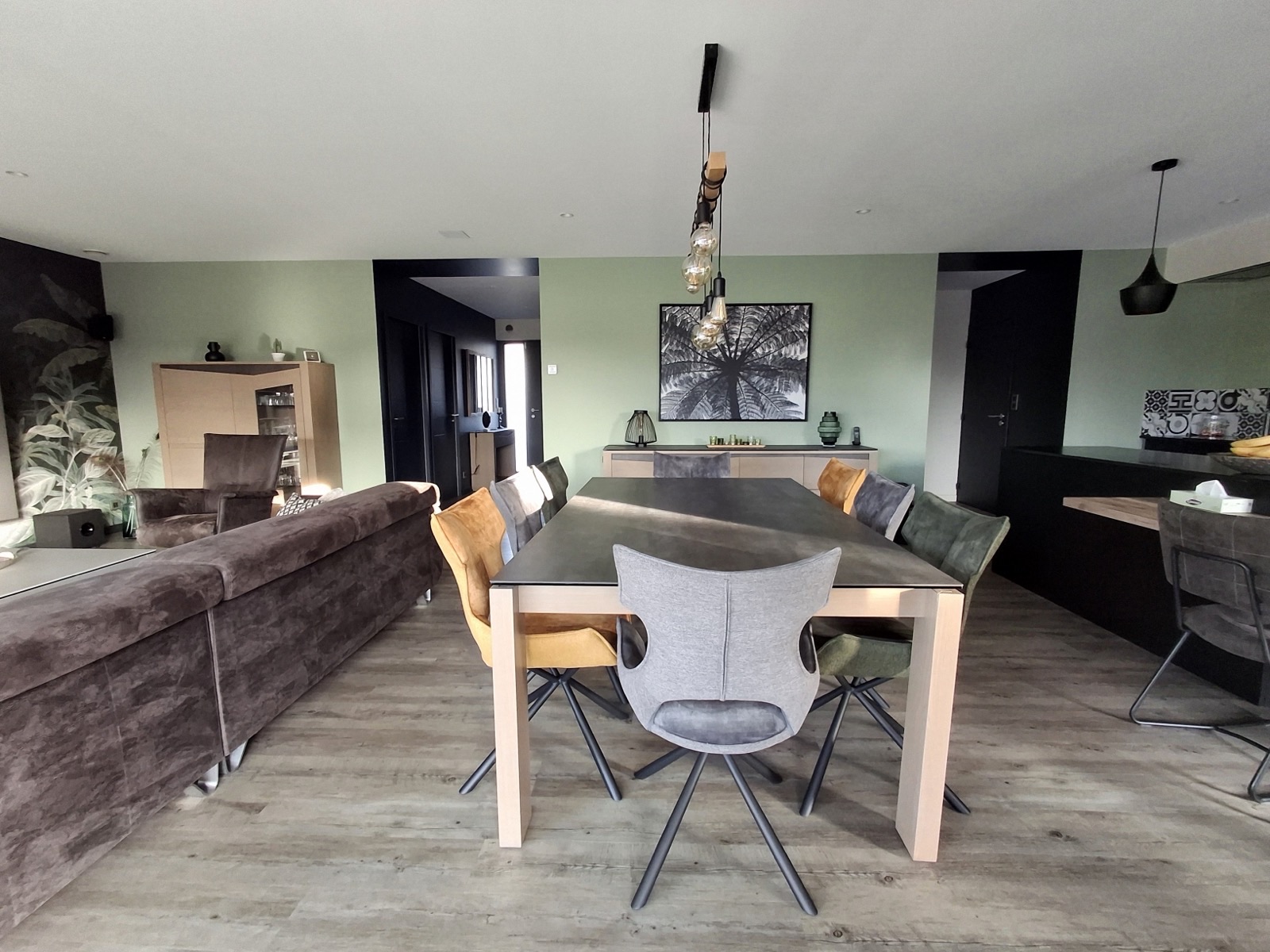 Séjour avec mur peint en vert, sol effet bois et grande table de salle à manger