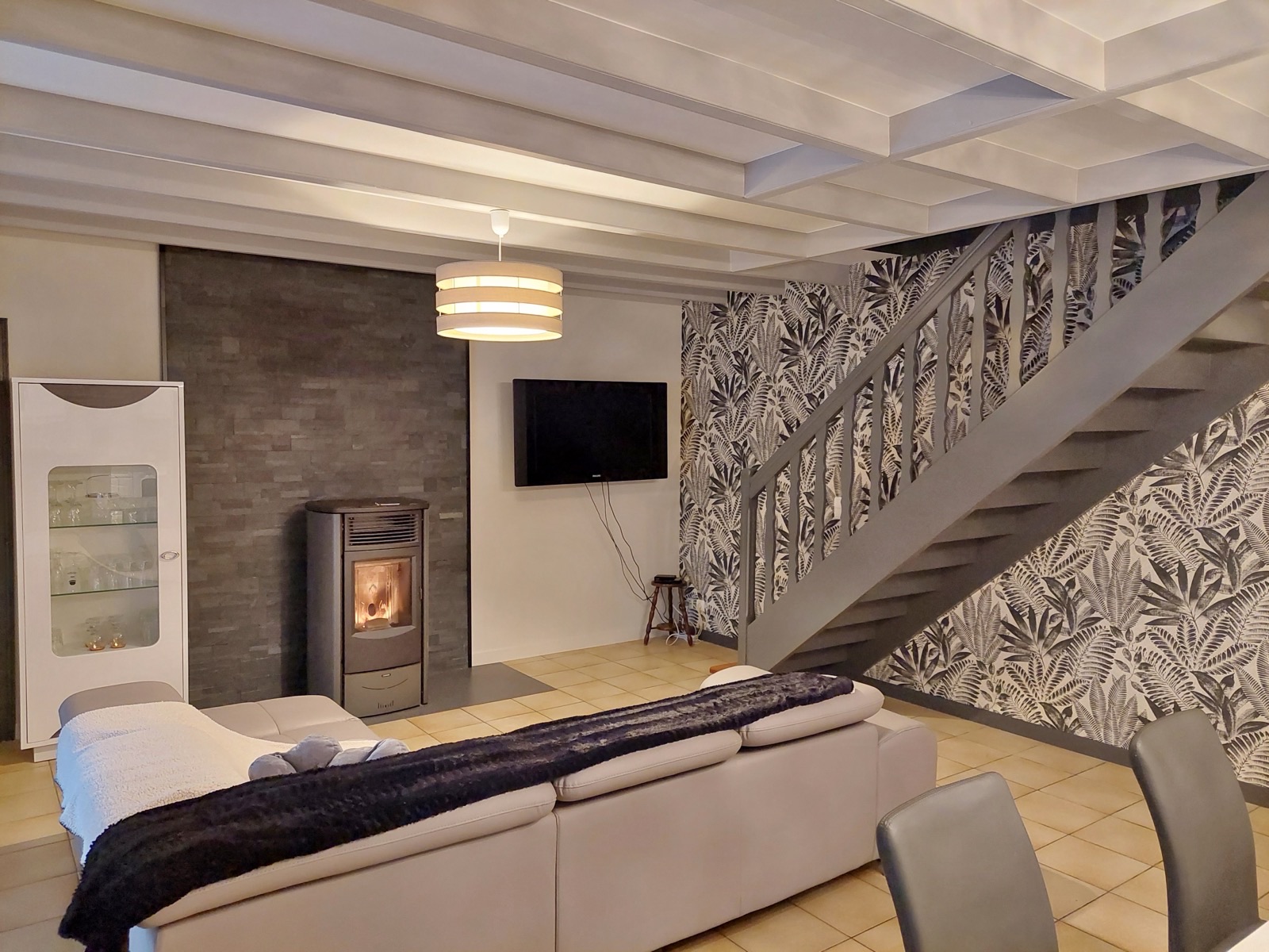 Poêle devant un parement gris foncé, escalier gris et papier peint feuillage noir et blanc