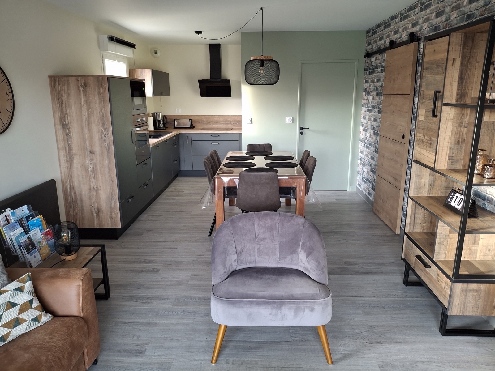 Séjour ouvert sur la cuisine, mur à effet brique gris et porte coulissante en bois
