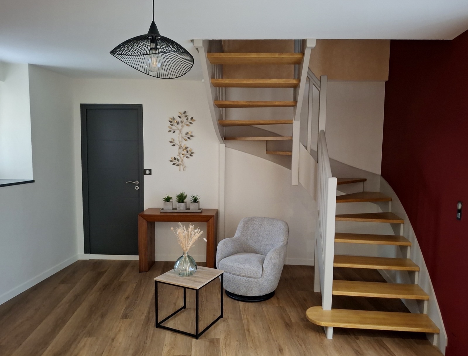 Entrée avec escalier blanc aux marches en bois clair, mur rouge et sol effet bois