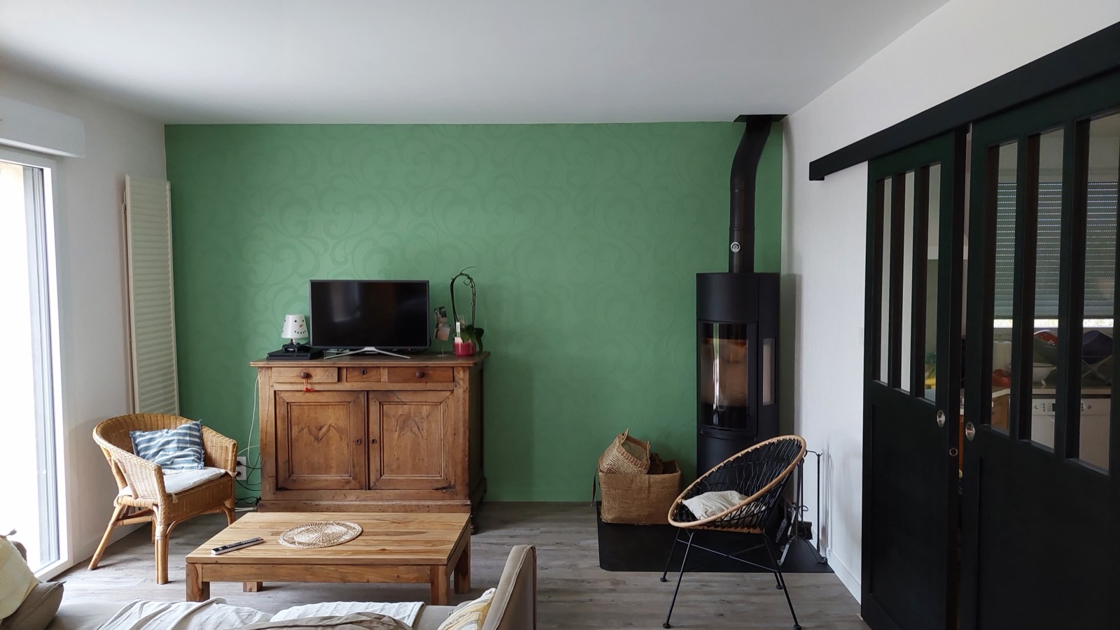 Salon avec mur vert à effet matière, buffet en bois et poêle noir